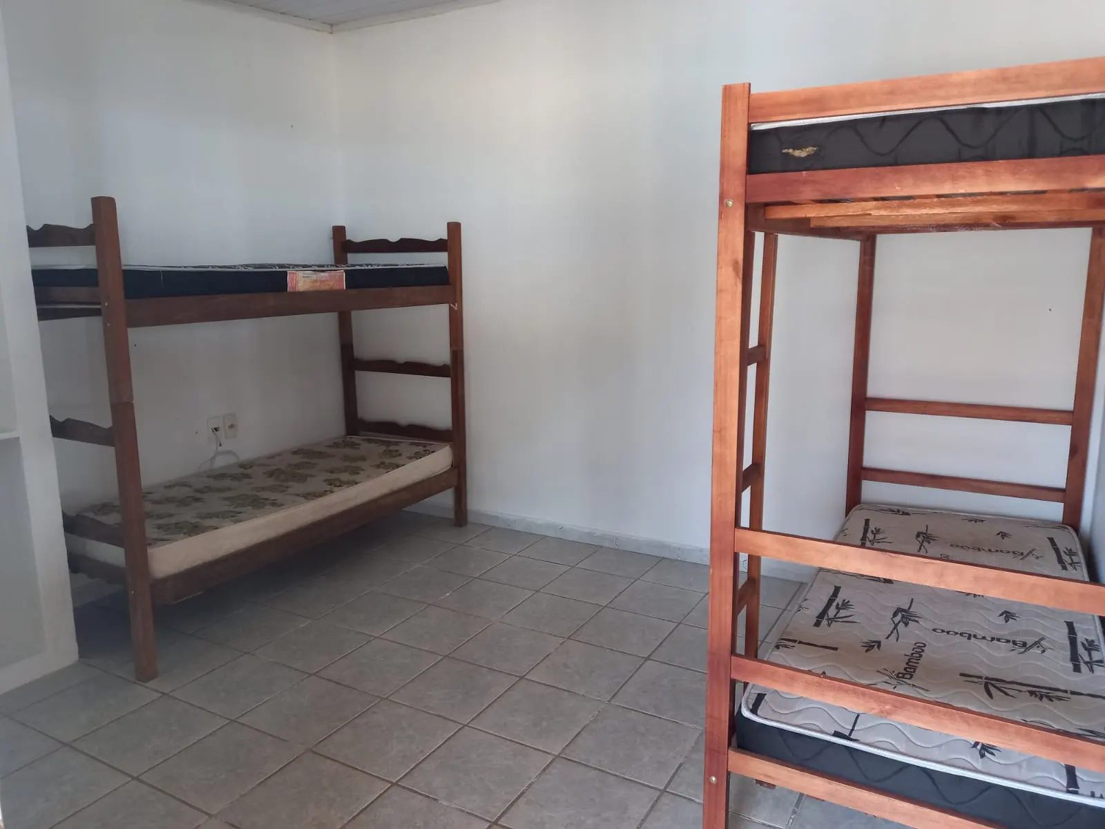 Quarto com beliches de madeira, colchões e piso claro.